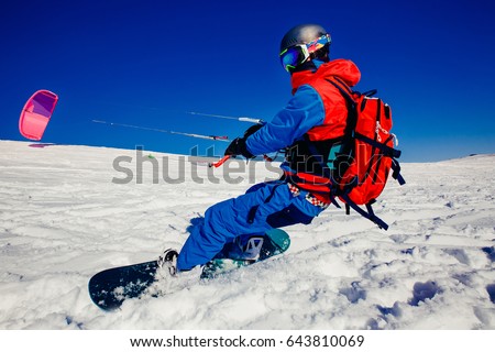 Snowboarder with a kite on fresh snow in the winter in the tundra of Russia against a clear blue sky. Teriberka, Kola Peninsula, Russia. Concept of winter sports snowkite. Royalty-Free Stock Photo #643810069
