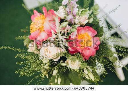 A composition of flowers and greens in a vase stands among the chairs for guests in the area of the wedding ceremony