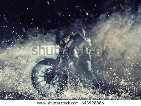 Detail of high power motorcycle chopper with man rider at night. Fog with backlights on background. Water splash on foreground Royalty-Free Stock Photo #643998886