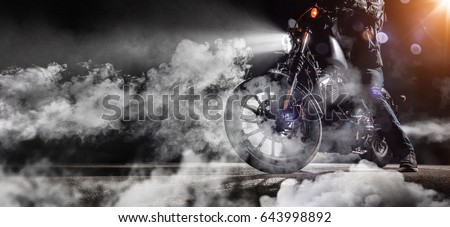 Close-up of high power motorcycle chopper with man rider at night. Fog with backlights on background.