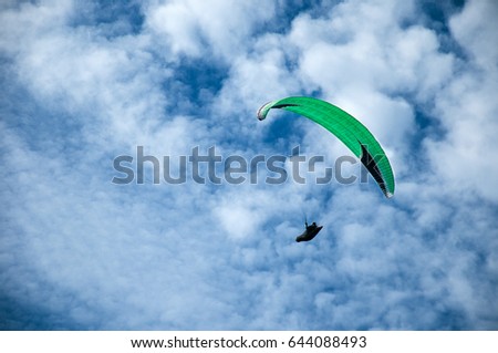 Green paraglider flying in the blue sky against the background of clouds. Paragliding in the sky on a sunny day.