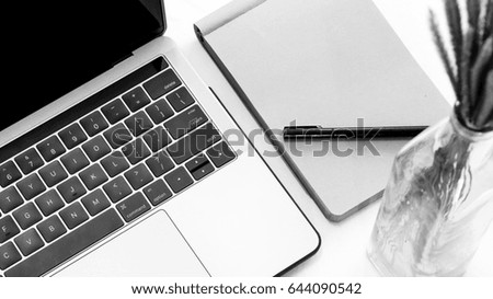 Laptop and notebook on white table,monochrome
