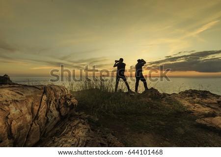 Two photographers are standing on the rock near the cliff to take a photo sunset