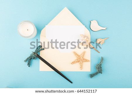 Layout of yellow envelope with white note card, calligraphy pen, candle, sea star, sea shells and bird on blue background.  Top view and flat lay with copy space. Minimal nautical concept.
