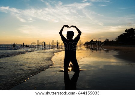 Silhouette of young boy making heart sign with his arms on the beach 
