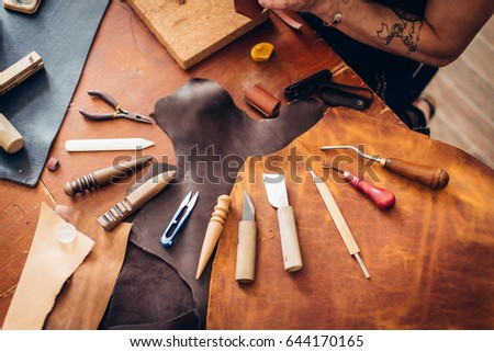 Leather craft tools on a wooden background. Leather craftmans work desk . Piece of hide and working handmade tools on a work table.