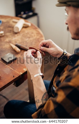 portrait of muscular middle eastern man wearing creative cup focused on work, while creating leather designs in workshop studio