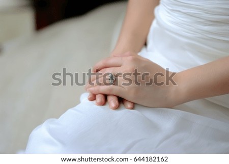 Bride on her white wedding dress holding hand with engagement ring sitting in a room