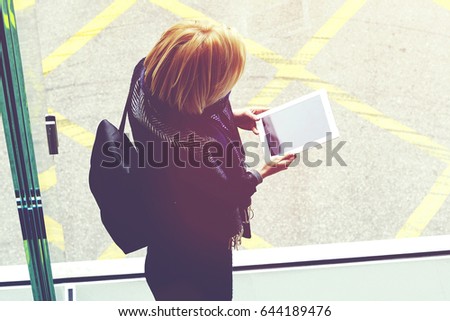 Top view of a woman with rucksack on her back is using touch pad for ordering o-nline place in a restaurant for dinner. Hipster girl is holding digital tablet with copy space screen for your content