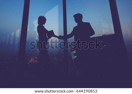 Silhouette of businessman shaking hands in honor of the transaction with his new woman partner, male and female entrepreneurs congratulate each other with their successful work Royalty-Free Stock Photo #644190853