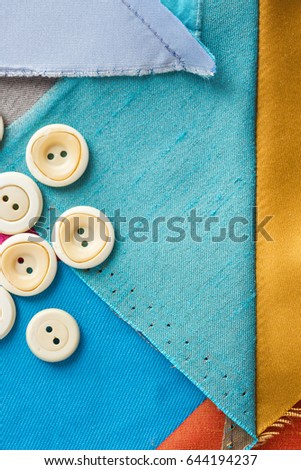 sewing, patchwork, tailoring and fashion concept - macro of desktop designer with white buttons and scraps of colored tissue, patches of blue, gray fabric, flat lay, top view, vertical