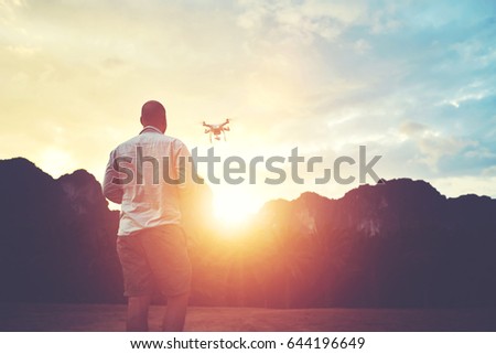 Silhouette of a man photographer is shooting video with multirotor RC quadcopter, while is standing against sunset and alp. Young male is taking photo on modern flying remote camera during summer trip