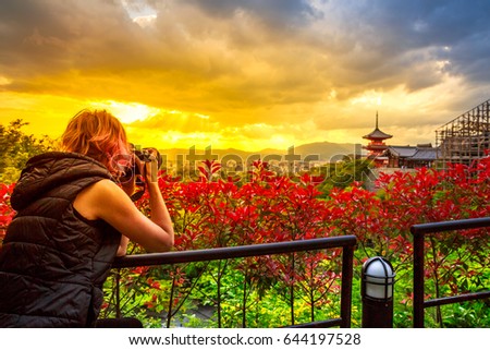 Travel woman photographer with professional camera takes shot of Kiyomizu-dera Temple with red pagoda at sunset light in spring time. Scenic aerial cityscape of Kyoto, Japan. Asian traveler concept.