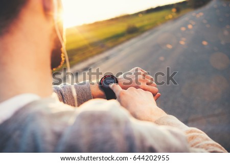 Young athlete runner in headphones looks at a modern smart clock and counts up spent calories after training outdoors at sunset Royalty-Free Stock Photo #644202955