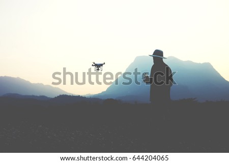 Silhouette of a man wanderer is shooting video on flying quadcopter camera by using remote controller. Young hipster gut is using RC aerial drone during his amazing summer adventure overseas