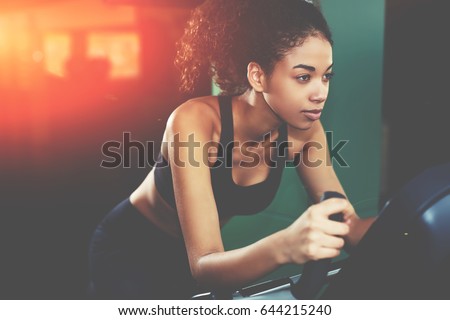 Attractive young woman at the gym riding on spinning bike. Confident afro American woman cycling on gym machine bicycle. Motivation and sporty goal concept Royalty-Free Stock Photo #644215240