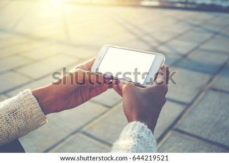 Cropped image of woman's hands holding cell telephone with blank copy space screen for your text message or advertising content, female watching video on smart phone while relaxing in the fresh air 