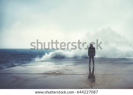Feeling of freedom, back view of adult man standing on pier facing to the sea with big waves beats against the shore on a cloudy autumn day, alone depress person,the power of nature, storm on seashore Royalty-Free Stock Photo #644227087