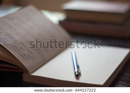 Open Notepad with handwritten notes with blue pen books in the background