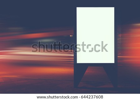 Illuminated blank billboard with copy space for your text message or content, public information board with shutter speed on background, advertising mock up in urban setting, empty poster on roadside 