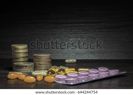 Roll of coins and pills with black wood background on wood floor.