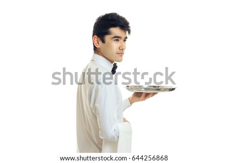 the young waiter with black hair and a white shirt stands sideways and holding in his hand the empty tray
