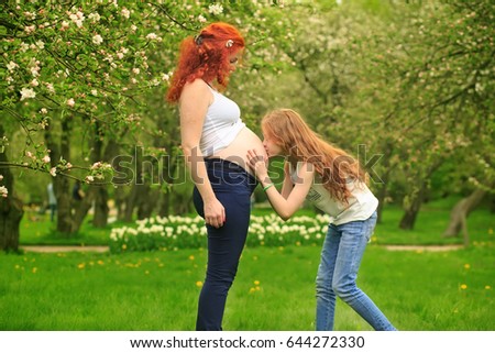 The daughter kisses a stomach of pregnant mother in the blossoming garden