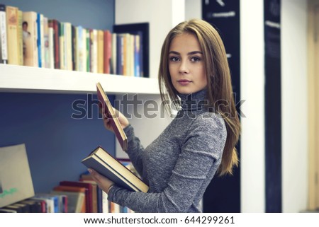 Portrait of confident beautiful teen girl standing in university library and searching interesting literature for improving personal skills and knowledge,charming young woman enjoy leisure time
