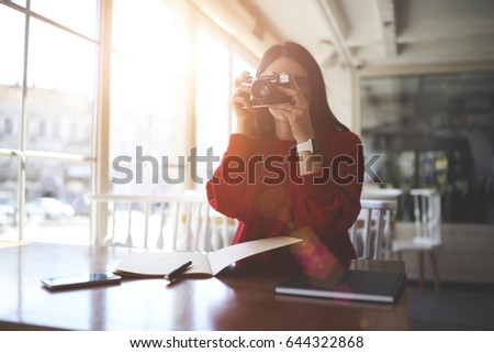 Creative journalist making photos of coffee shop interior for writing interesting article in notebook about new interesting urban places.Female photographer taking picture during studying indoors