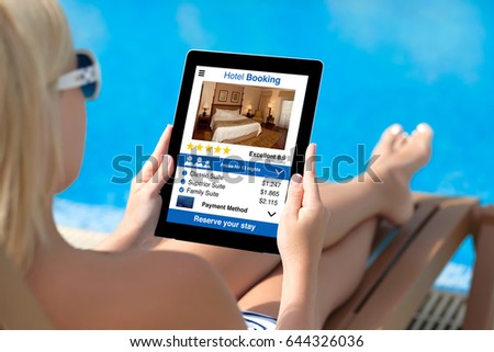 woman on sun lounger by pool holding tablet with app hotel booking screen