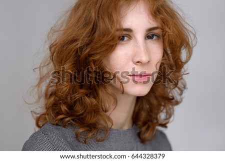 A red-haired girl with freckles looks ahead. Expression of a person without emotions.