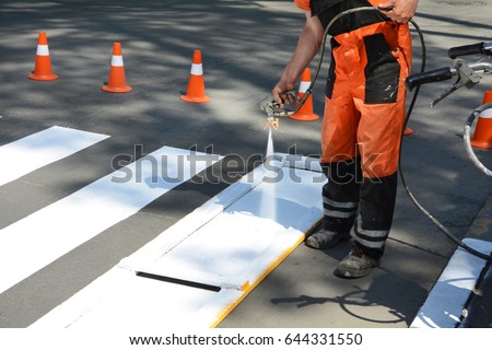 Worker is painting a pedestrian crosswalk.