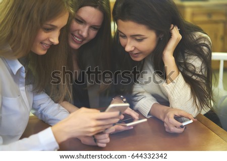 Cropped image of beautiful best friends with smile reading funny comments under videos in own blog on modern smartphone device using free 4G internet connection during break sitting indoors