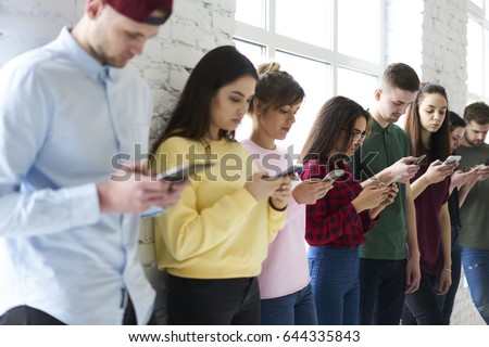 Crew of male and female coworkers spending work break browsing and surfing internet using modern digital devices ignoring conversation in real life,concept young people having addiction to smartphones
