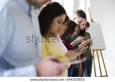 Young male and female students ignoring real life communication chatting in social networks using application on modern digital devices, hipsters in casual wear spending free time surfing internet