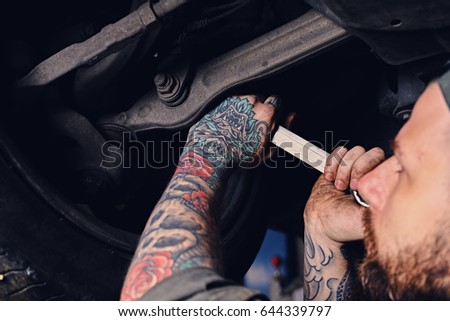 Bearded tattooed mechanic balancing car's wheel in a workshop.