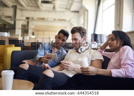 Afro american male internet user showing mobile application for making funny photos on modern telephone devices to friends enjoying leisure and free time during coffee break sitting in loft interior