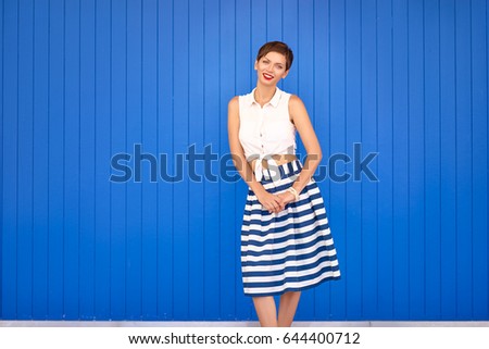 Striped and colorful. Haircut and red lipstick make up. Portrait of smiling young woman. Blue background.