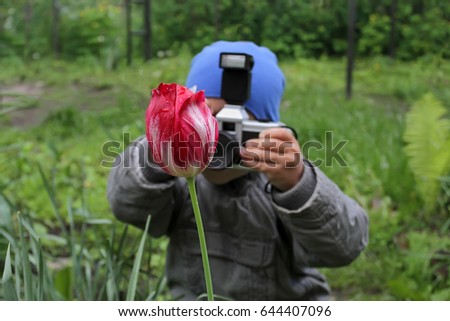 Little boy is taking pictures of a red tulip flower. Babe irers in the photographer in role-playing games of great importance in the development of children. A young photographer takes a flower.