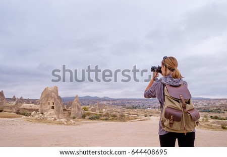 Traveling and photography. Young woman with camera and backpack taking picture at Cappadocia, Turkey.