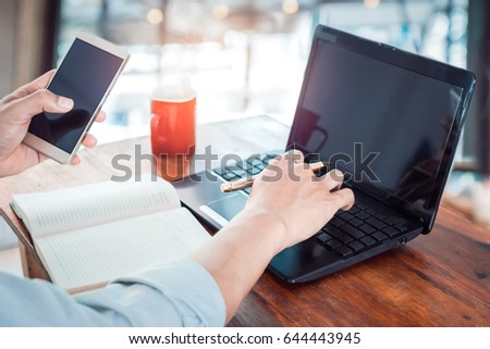The lifestyle of office workers - young businessman hands typing on his laptop. Businessmen working at modern business office and using mobile smartphone with red coffee cup. vintage color filter.