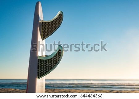 Enhanced, colourful image of surfboard fins at the beach with low sunlight.
