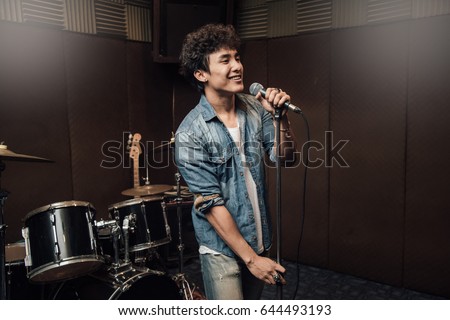Male lead vocalist singing in studio with music instrument background. Royalty-Free Stock Photo #644493193