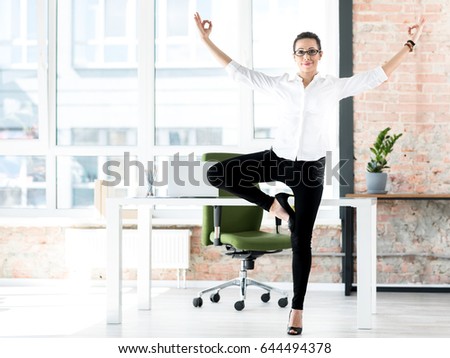 Half length happy woman making exercise at job. She standing in wide modern office