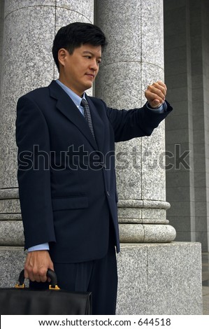 Asian Man in A Business Suit Standing outside A Building And Looking At The Time