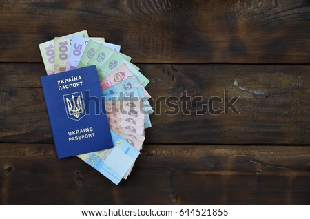 A photograph of a Ukrainian passport and a certain amount of Ukrainian money on a wooden surface. The concept of making money for Ukrainian citizens abroad