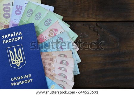 A photograph of a Ukrainian passport and a certain amount of Ukrainian money on a wooden surface. The concept of making money for Ukrainian citizens abroad