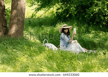 Summer time. Young woman in a forest at a picnic taking pictures of herself on a smart phone. Selective focus