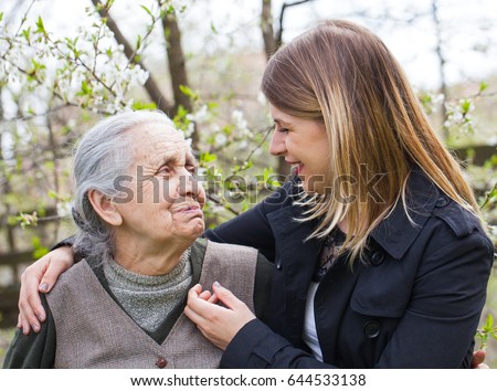 Picture of an elderly woman with cheerful caregiver outdoor in the garden, springtime