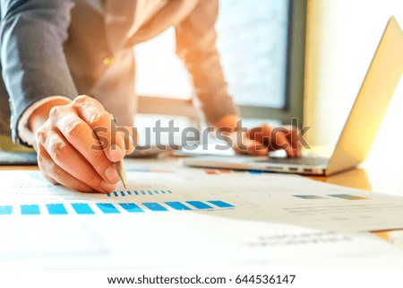 Businessman is using a laptop and a pen to analyze data from the graph on the desk,The concept of using internet with laptop to analyze data,Concept graphical analysis and data recording with laptop.